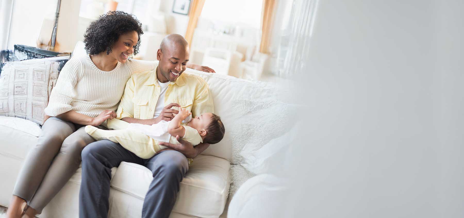 Smiling father feeding baby on sofa